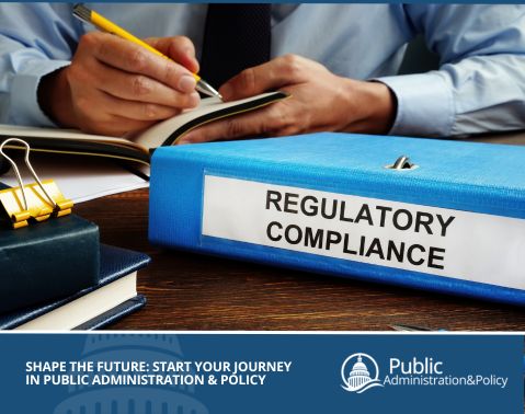 Person at a desk writing in a notebook with a binder labeled regulatory compliance, symbolizing the role of public policy-making in enforcing rules and standards.